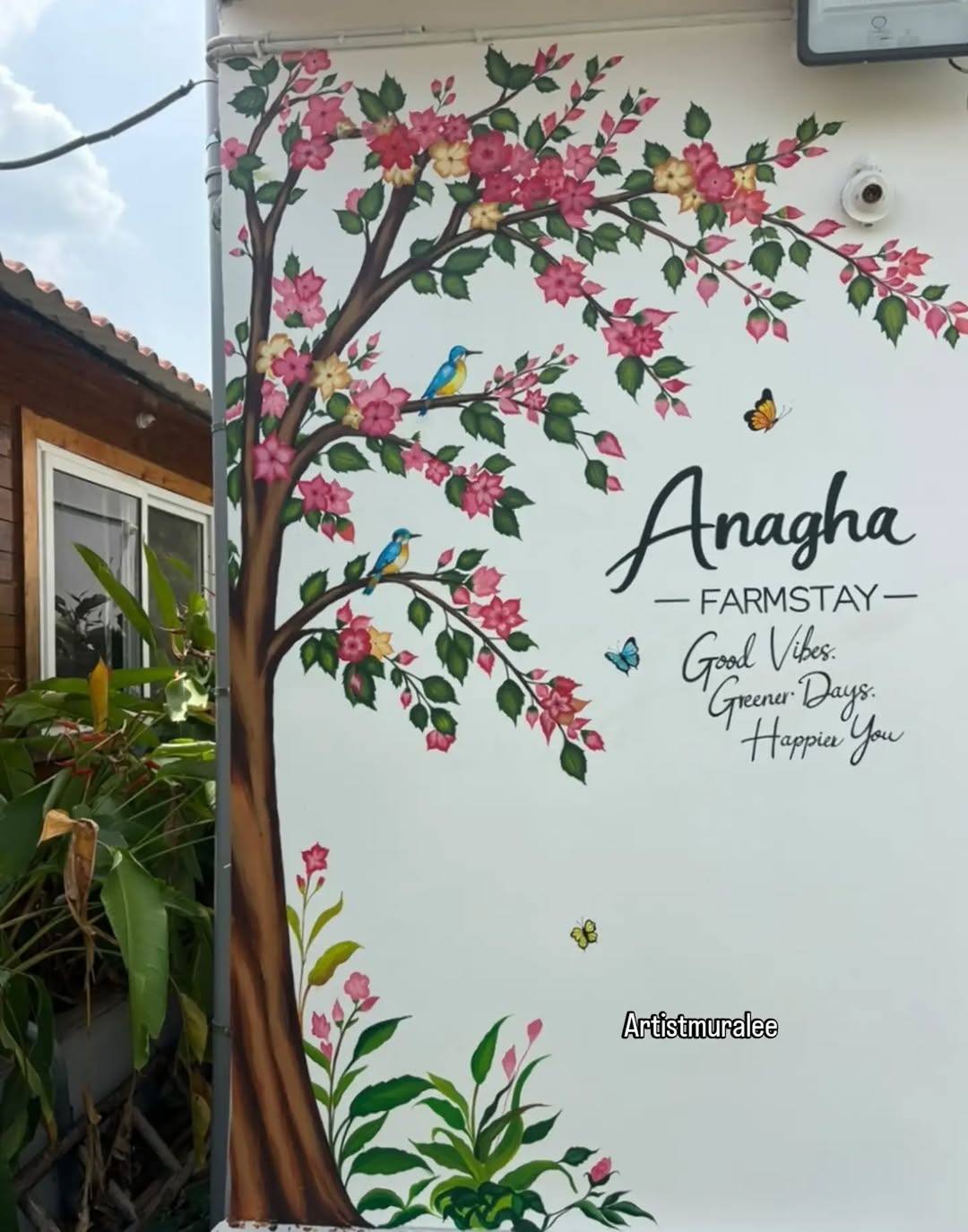 Large hand-painted exterior wall mural of a flowering tree with birds at Anagha Farmstay