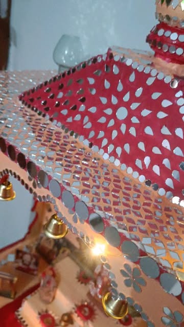 Close-up detail of handcrafted temple shikhar with mirror art and brass bells