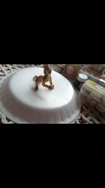Brass Bal Gopal idol on sculpted white pedestal during studio craft preparation