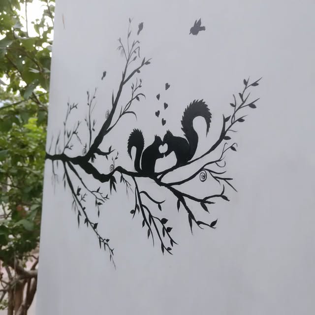 Hand-painted monochrome wall art showing a squirrel couple on a branch with hearts
